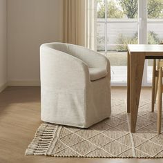 a white chair sitting in front of a window next to a wooden table and chairs