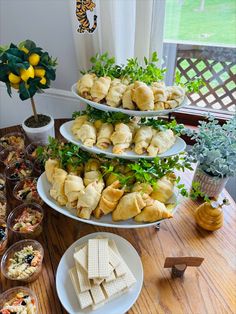 three tiered trays filled with food on top of a wooden table next to a potted plant