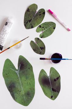 some green leaves are laying on the table next to paintbrushes and other crafting supplies