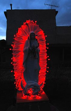 a statue with red lights around it in front of a building at night and the sky is dark