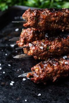 several meat skewers on a black surface with parmesan sprinkles