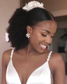 a woman in a white dress is smiling and looking at her cell phone while wearing a flower hair clip