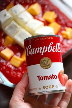 someone holding up a can of soup with cheese and tomato on it in front of a pan