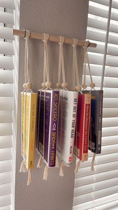 a row of books hanging from the side of a wall next to a window with white blinds