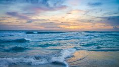 the sun is setting over the ocean with waves crashing on the shore and clouds in the sky