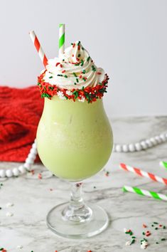 a green drink with white frosting and sprinkles in a glass next to candy canes