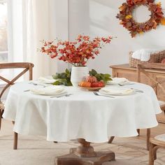 a dining room table set for two with fall decorations on the table and chairs around it