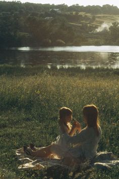 two women sitting in the grass near a lake