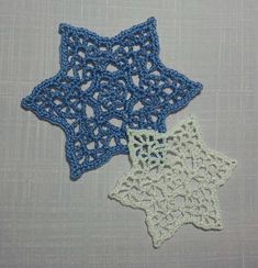 two crocheted stars are sitting on a gray tablecloth, one is blue and the other is white