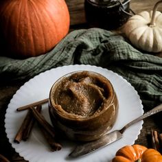 a bowl of pumpkin butter on a plate with some cinnamon sticks and two pumpkins in the background