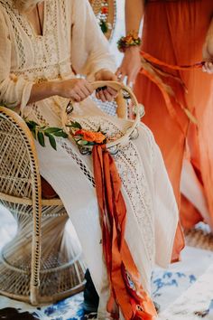 two women in orange dresses are sitting on wicker chairs and one is holding a basket