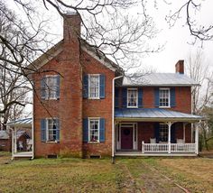 an old brick house with blue shutters on the front and side windows, surrounded by bare trees