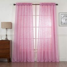 a pink curtain hanging on the side of a window next to a dresser and lamp