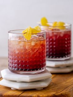 two glasses filled with drinks sitting on top of a wooden table next to each other