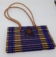 Thailand Purse Handbag Woven Straw Rattan Purple Handmade Flower Brown Womens This is a nice preowned purse handbag from Thailand.  This was a gift and was never used.  It is hand crafted with rattan and thread and grass.  It has a decorative flower on the front that hooks around and closes on the back.  It has a double handle that is woven.  Inside it is lined with black fabric and has one pocket and has a tag which says, "Made in Thailand". The purse without the strap measures approximately 5. Artisan Blue Rectangular Bag, Handmade Square Straw Bag For Gift, Blue Handwoven Bag As A Gift, Blue Bags With Bamboo Handle For Everyday Use, Handmade Blue Rectangular Beach Bag, Artisan Rectangular Straw Bag, Blue Everyday Bags With Bamboo Handle, Square Brown Straw Bag For Gift, Square Brown Straw Bag Gift