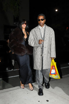 a man and woman walking down the street at night with one holding a bag in his hand