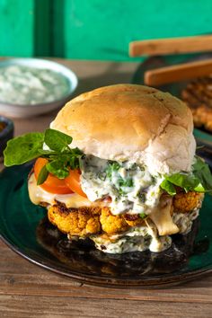 a chicken burger on a black plate with sauce and lettuce in the background