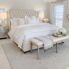 a white bedroom with a large bed, chandelier and two tables in front of it