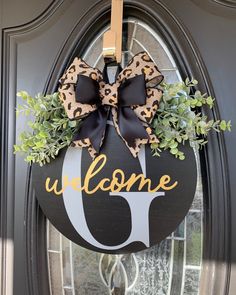 a welcome sign hanging on the front door with leopard print bow and green plants in it