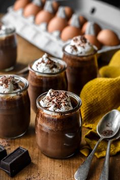 chocolate pudding with whipped cream on top and spoons next to eggs in the background