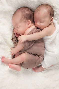 two babies cuddle together on a white blanket