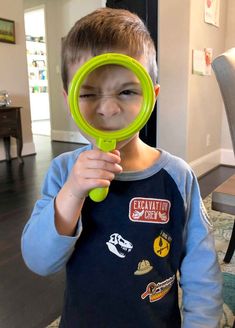 a young boy holding a magnifying glass in front of his face while looking at the camera