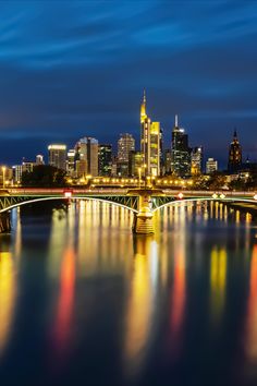 the city skyline is lit up at night with lights reflecting on the water and bridge