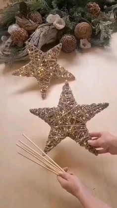 two star shaped candles are being held up by someone's hand and some pine cones in the background