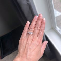 a woman's hand with a diamond ring on her left hand next to a window