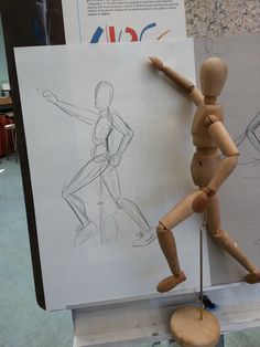 a wooden mannequin standing next to a drawing board