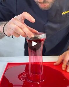 a man is pouring red liquid into a glass vase with his thumb on the top