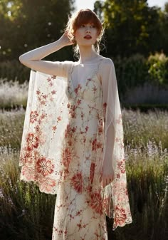 a woman standing in front of some flowers wearing a white dress with red flowers on it