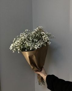 a person holding a bouquet of flowers in their hand against a wall with white walls