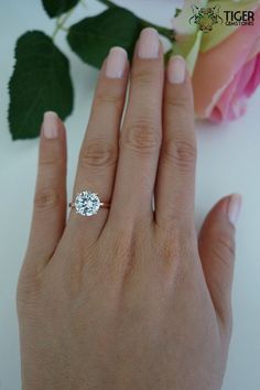 a woman's hand with a diamond ring on top of her finger next to a rose