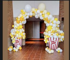 popcorn buckets filled with yellow and white balloons in front of an entrance to a movie theater