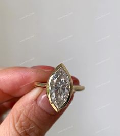 a woman's hand holding a gold ring with a diamond in the middle and a white background