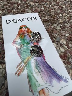 a card with a drawing of a woman in a dress holding an umbrella and the words demeter on it