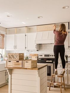 a woman standing on top of a kitchen counter next to a wooden box filled with boxes