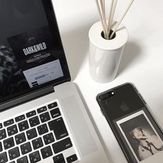 an open laptop computer sitting on top of a white desk next to a cell phone