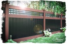 a wooden fence with black privacy panels and green grass in the foreground, sunlight shining through trees