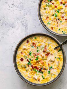 two bowls filled with corn and bacon soup on top of a table next to a spoon