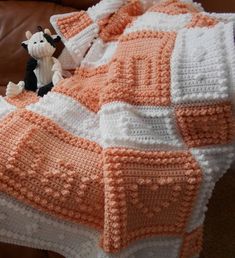 an orange and white crocheted blanket sitting on top of a brown leather couch