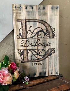 a wooden sign sitting on top of a table next to flowers and a vase with pink roses