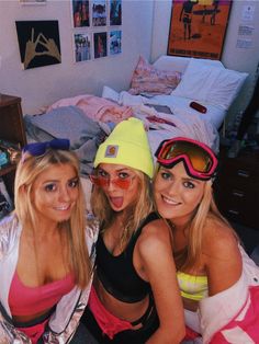 three beautiful young women sitting next to each other in front of a bed wearing ski goggles