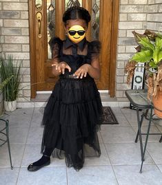 a woman in a black dress and yellow face paint sitting on the front steps of a house