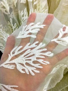 a person's hand with white embroidered designs on it and some flowers in the background