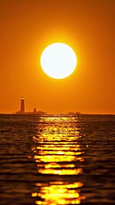 the sun is setting over the ocean with a lighthouse in the distance