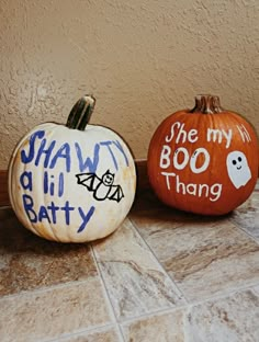 two painted pumpkins sitting on top of a tile floor next to each other with words written on them