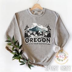 "Whether you're looking for a gift for her or a gift for him, this versatile, oversized crewneck sweatshirt is the ideal choice for anyone seeking the perfect fusion of fashion and function. This unisex pullover is not just a clothing item; it's a statement piece that proudly showcases the picturesque allure of Oregon's majestic mountains.  Whether you're hiking through Oregon's untamed wilderness or embarking on a cross-country road trip, this versatile Oregon sweatshirt is your ideal companion. It not only celebrates the rugged beauty of the state's mountains but also encapsulates the spirit of every hiking enthusiast and travel lover. Unisex Heavy Blend™ Crewneck Sweatshirt - Oregon Sweatshirt Ideal for any situation, Unisex heavy blend crewneck sweatshirt will keep you warm during the Outdoor Crew Sweatshirt With Graphic Print, Outdoor Graphic Print Crew Sweatshirt, Outdoor Crew Neck Sweatshirt With Graphic Print, Outdoor Long Sleeve Sweatshirt With Screen Print, Long Sleeve Sweatshirt With Screen Print For Outdoor, Cotton Adventure Sweatshirt With Letter Print, Long Sleeve Graphic Print Sweatshirt For Adventure, Winter Adventure Crew Neck Sweatshirt, Winter Crew Neck Sweatshirt For Adventure