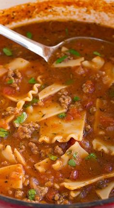 a red pot filled with pasta and meat soup on top of a white wooden table